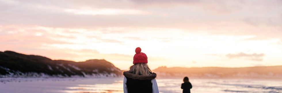 back-view-of-a-woman-walking-on-a-beach-at-sunset-in-winter