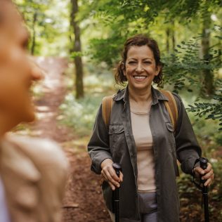 Two friends enjoying hike in forest with hiking poles